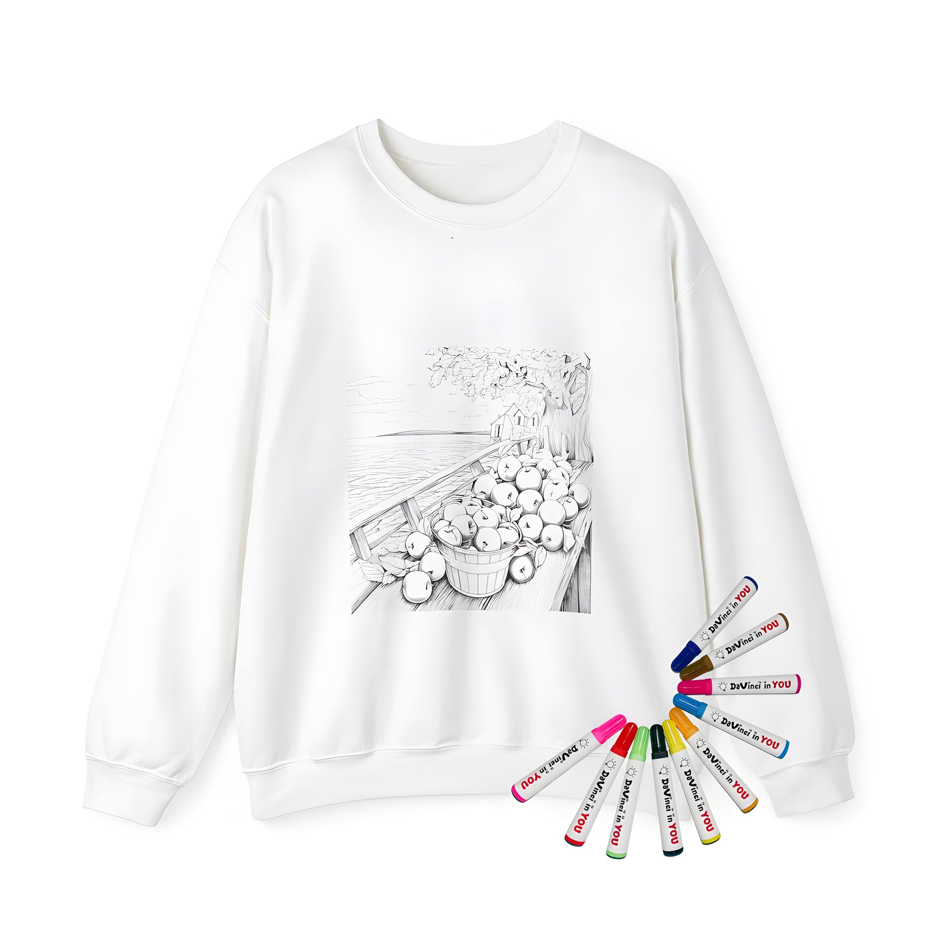 Adult sweatshirt featuring a unique coloring page design with a black and white illustration of apples in a bucket on a dock by a tree, including a house and lake in the background. Perfect for fall enthusiasts who love harvest themes.