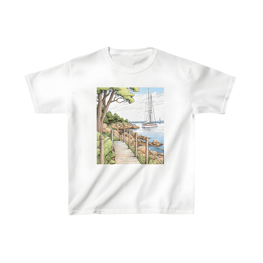 Colorful kid's t-shirt with coastal landscape print featuring wooden path, greenery, rocky shore, calm ocean waters, and sailboats.